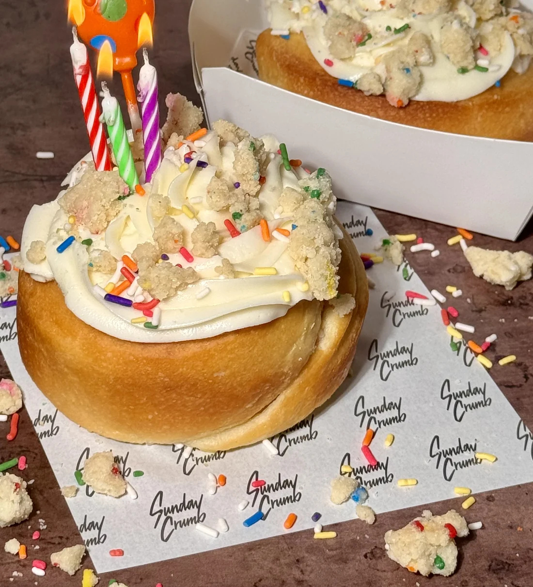 A real Sunday Crumb birthday cinnamon roll, sprinkles and frosting, on branded tissue paper